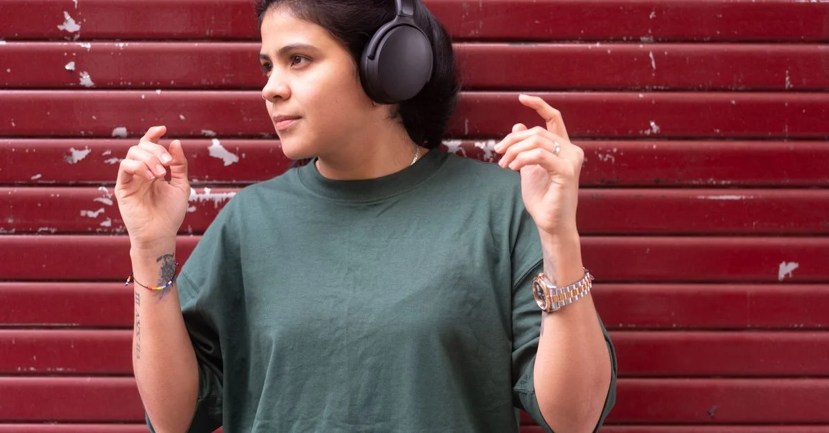 Femme en t-shirt vert écoutant de la musique avec des écouteurs contre un mur rouge.