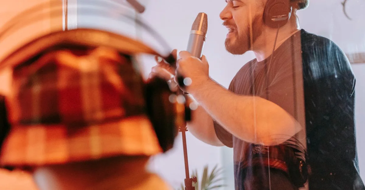 Chanteur masculin adulte enregistrant des voix dans un studio, portant des écouteurs et utilisant un microphone.