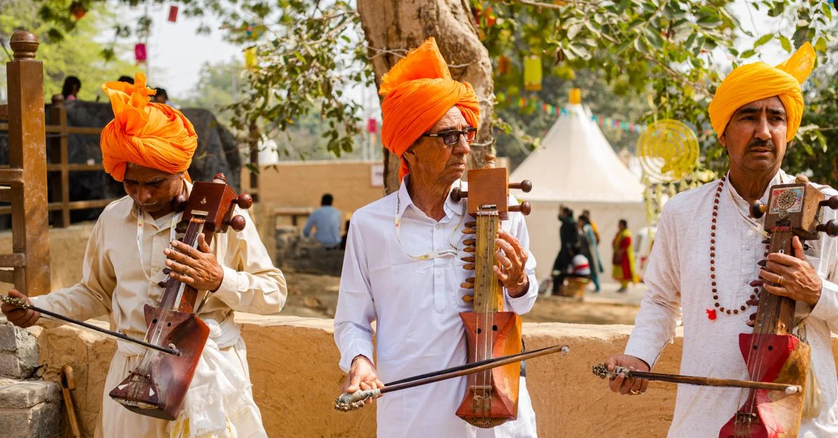 Trois musiciens du Rajasthan jouent d'instruments traditionnels en plein air, portant des turbans vibrants.