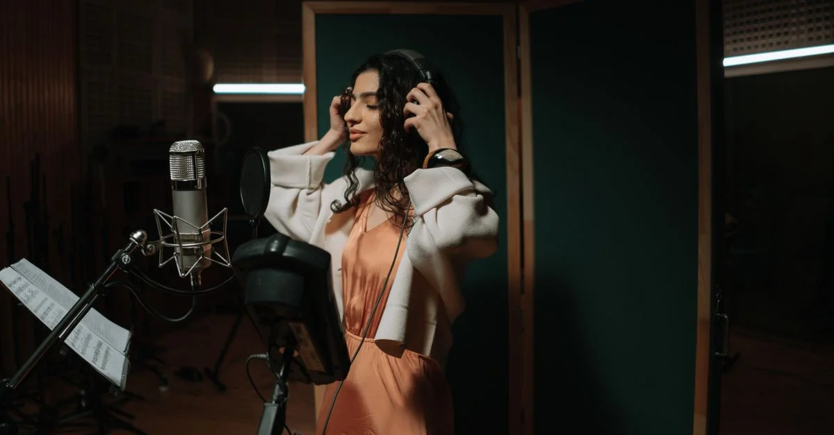 Chanteuse enregistrant de la musique dans un studio professionnel portant des écouteurs et utilisant un micro.