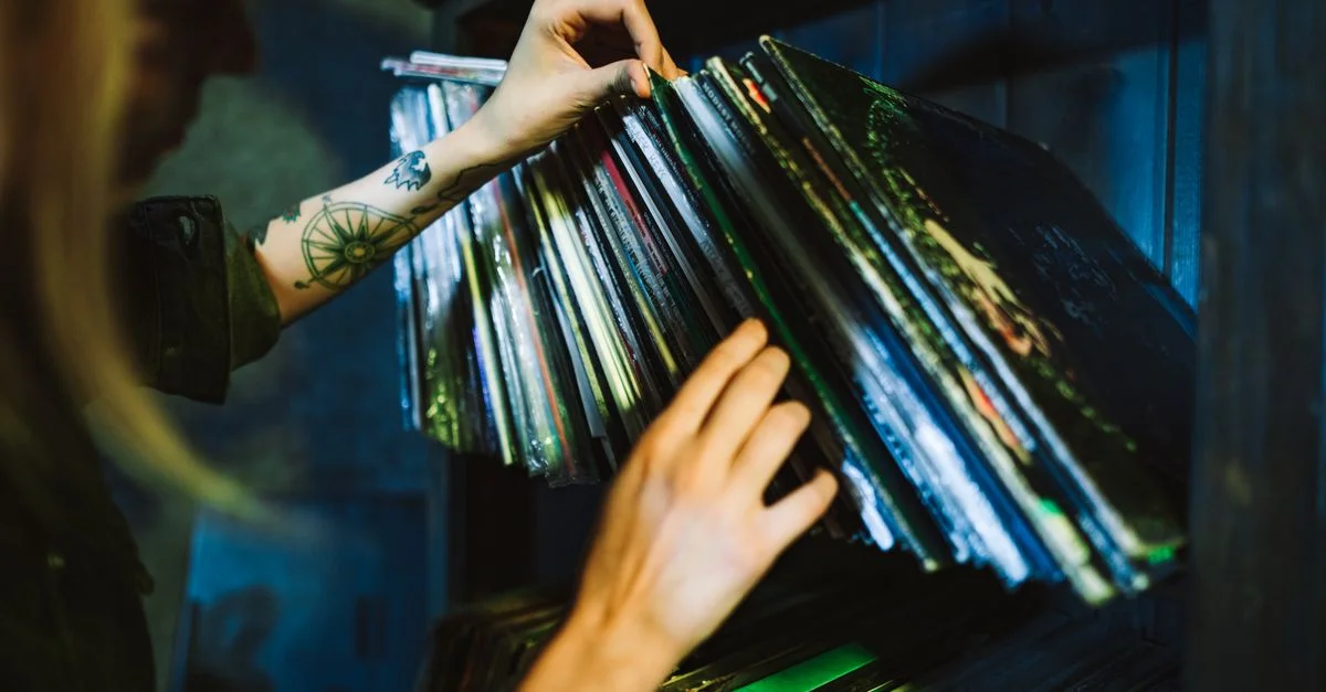 Gros plan sur une femme choisissant des disques vinyles sur une étagère avec un bras tatoué.