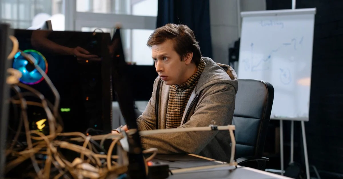 Jeune homme intensément concentré sur son travail informatique dans un bureau technologique avec un tableau blanc en arrière-plan.