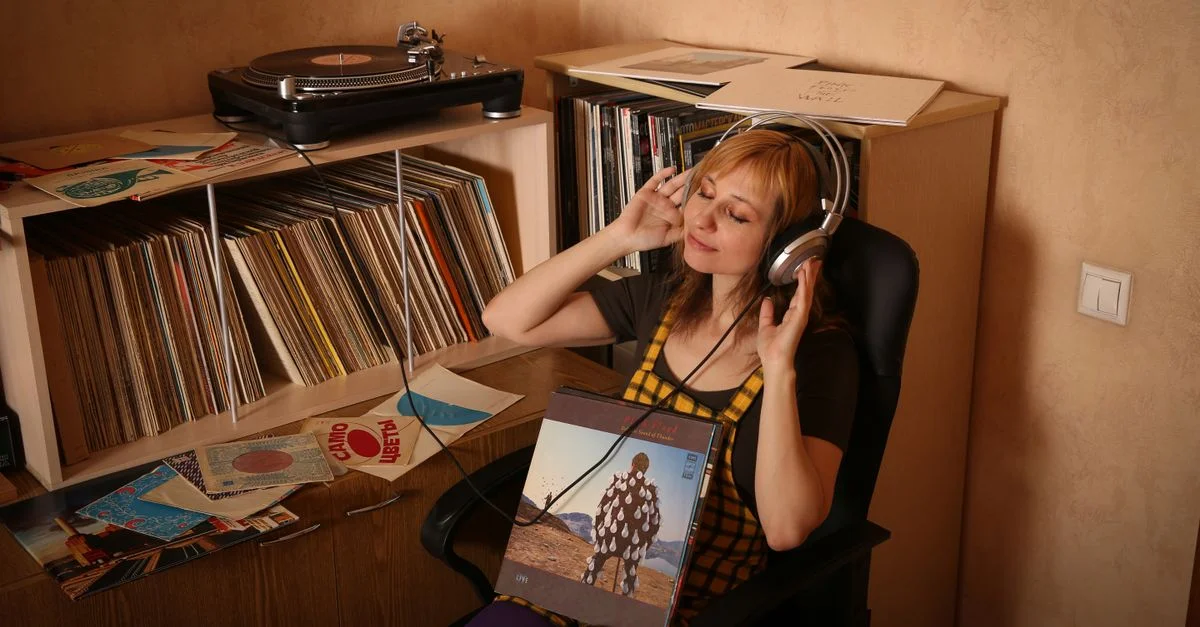 Femme assise avec des écouteurs, entourée de vinyles, profitant de la musique dans un cadre vintage.