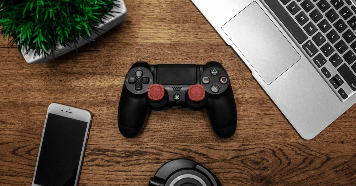 Une photo en plongée présentant une console de jeu, un ordinateur portable, un smartphone et des écouteurs sur une table en bois.