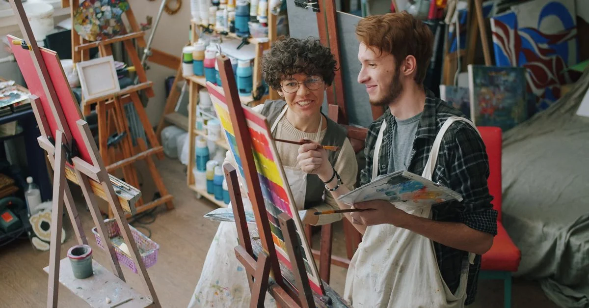 Deux artistes peignent ensemble dans un atelier vibrant rempli de matériaux.