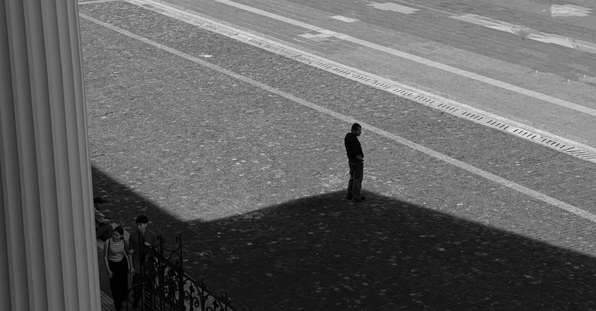 Homme solitaire debout dans l'ombre, rue urbaine, photographie en noir et blanc.