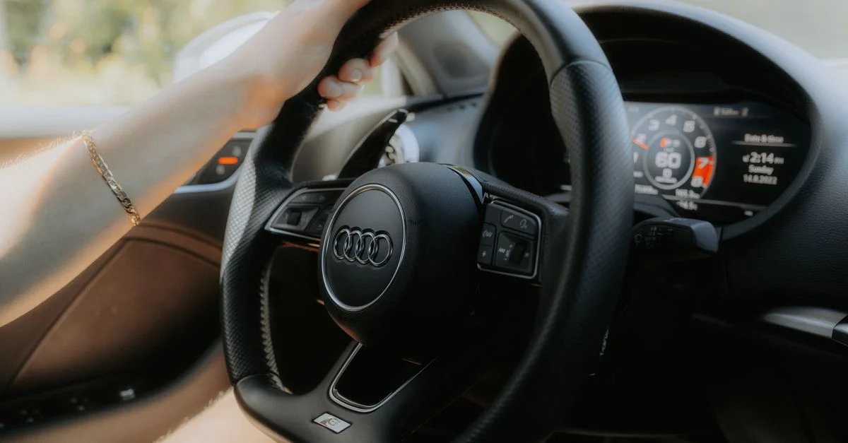 Un gros plan détaillé d'une personne tenant le volant d'une Audi, mettant en valeur l'intérieur de la voiture.