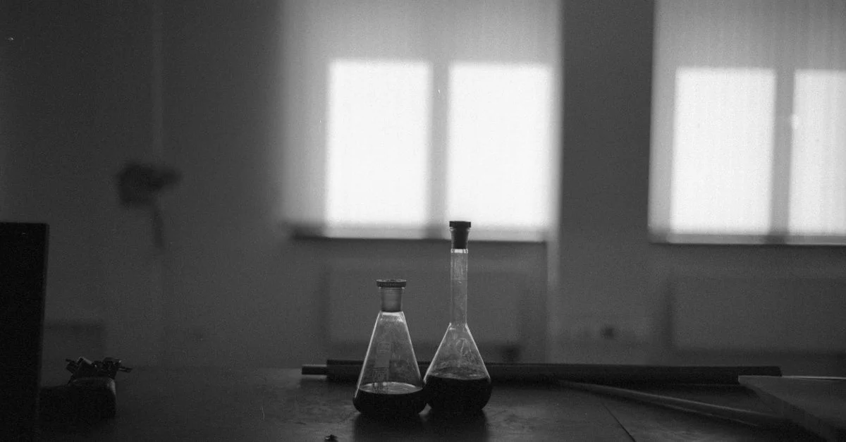 Image monochrome de flacons de laboratoire avec des bouchons sur une table sombre dans une pièce bien éclairée.