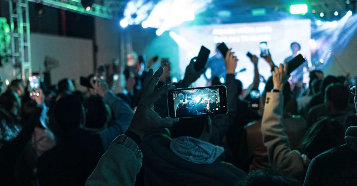 Une foule animée capturant des moments de concert sur des smartphones, des lumières vibrantes créent une atmosphère dynamique.