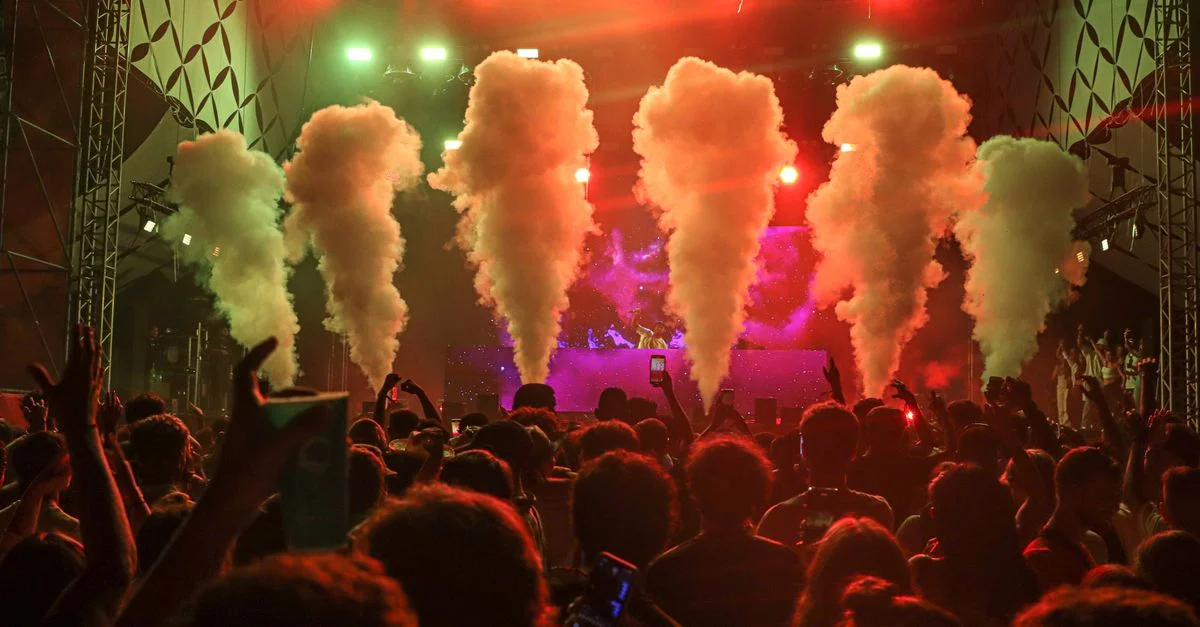 Concert bondé avec des lumières vibrantes et des effets de fumée créant une atmosphère énergique.