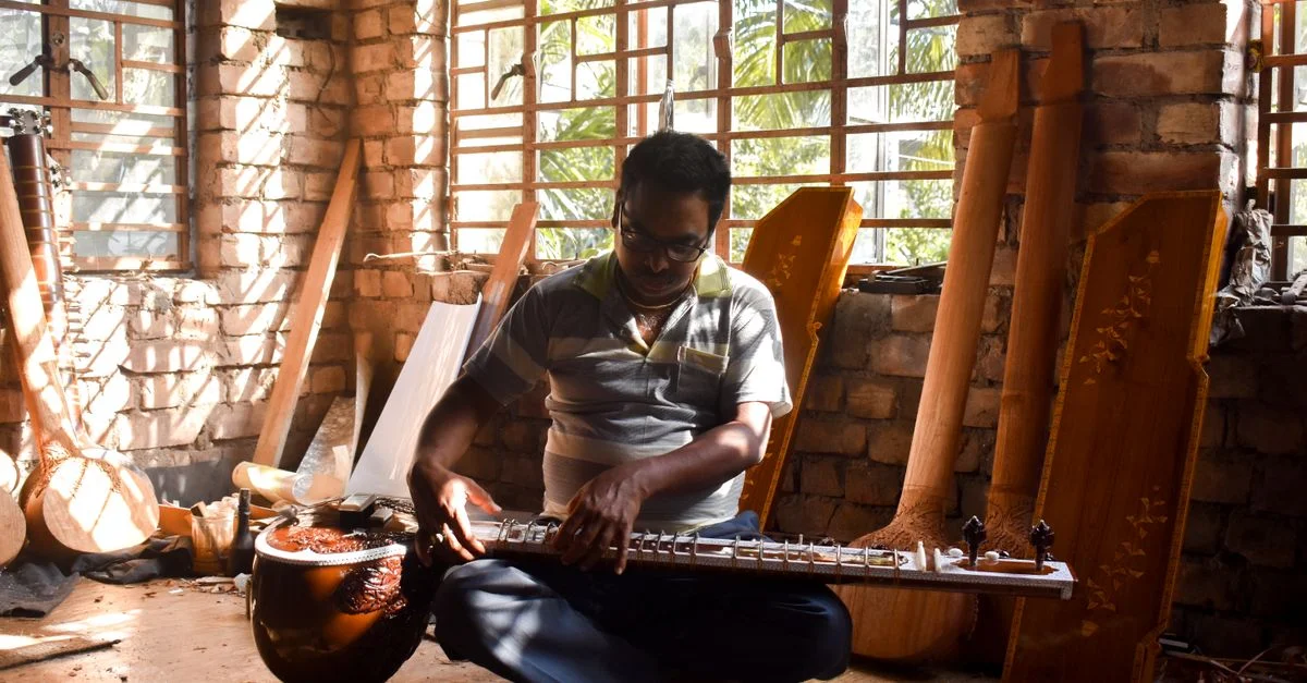 Artisan à Kolkata, en Inde, fabriquant un instrument de musique traditionnel dans une pièce ensoleillée.