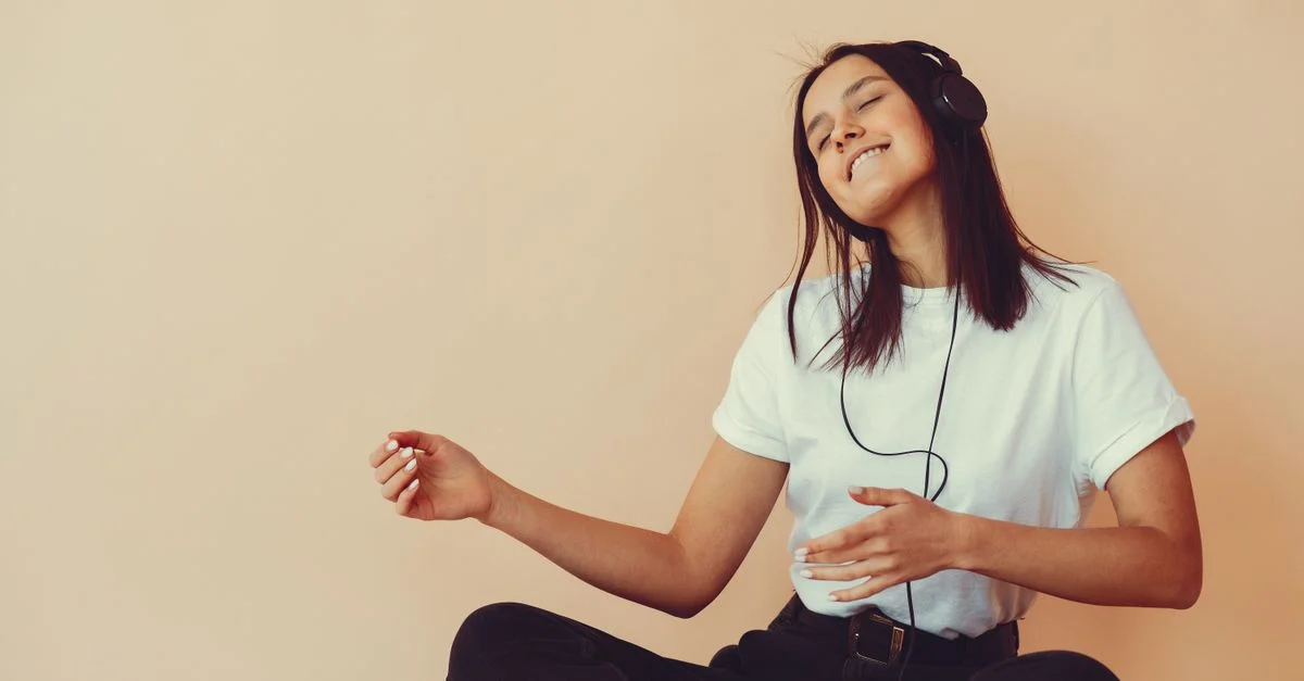 Une femme heureuse, les yeux fermés, écoute de la musique avec des écouteurs dans un cadre de studio.