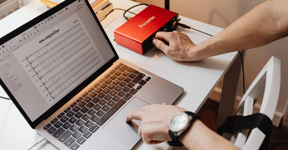 Vue rapprochée d'un ordinateur portable affichant une composition musicale à côté d'une interface audio sur un espace de travail.