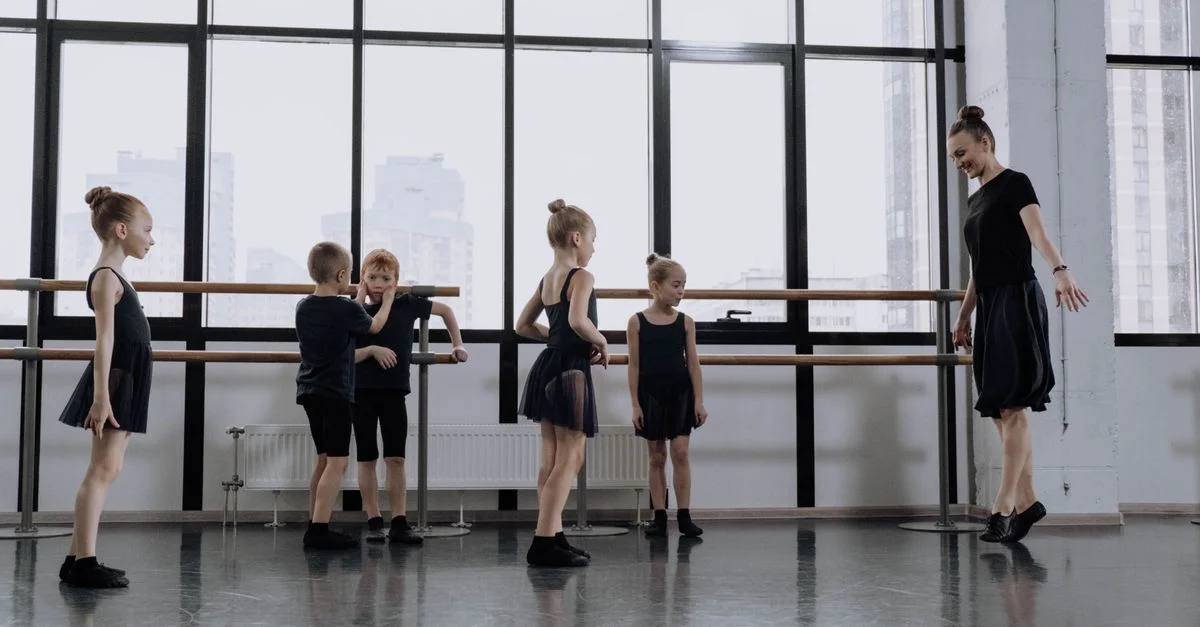 De jeunes enfants apprenant le ballet dans un studio de danse avec des fenêtres du sol au plafond et un instructeur de ballet.