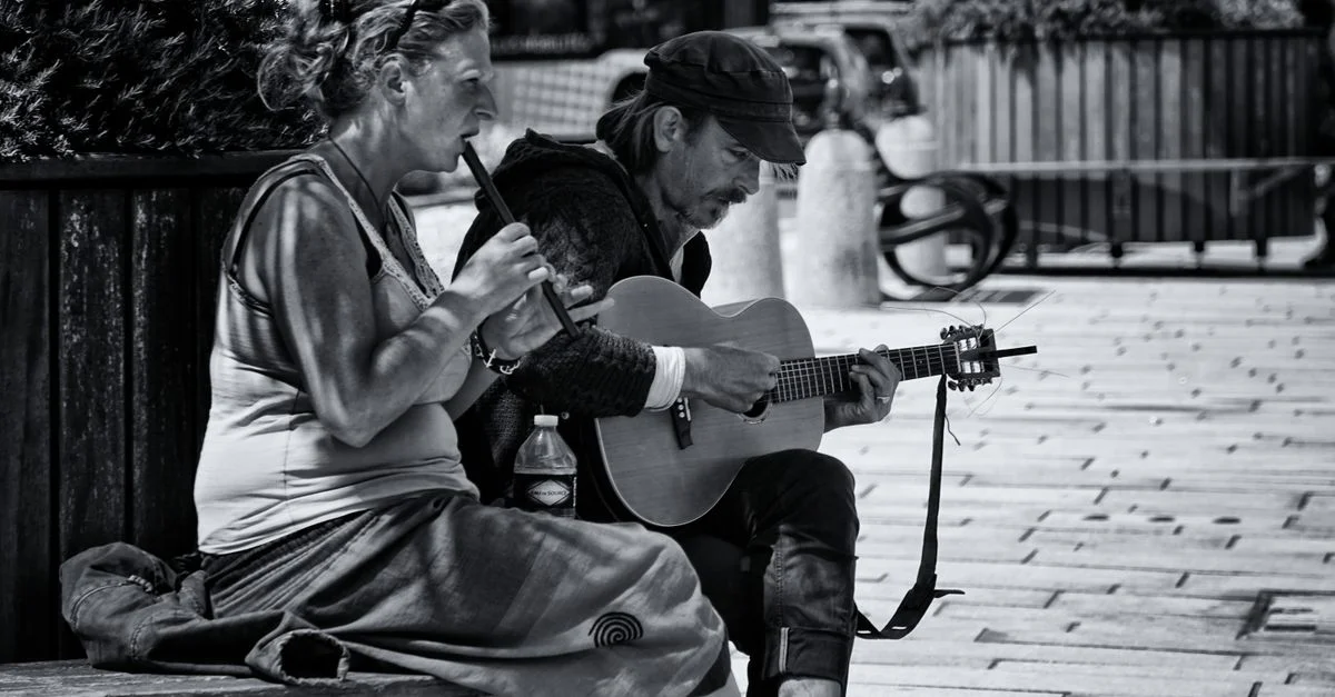 Une image en noir et blanc de musiciens de rue jouant de la guitare et de la flûte dans un cadre urbain.