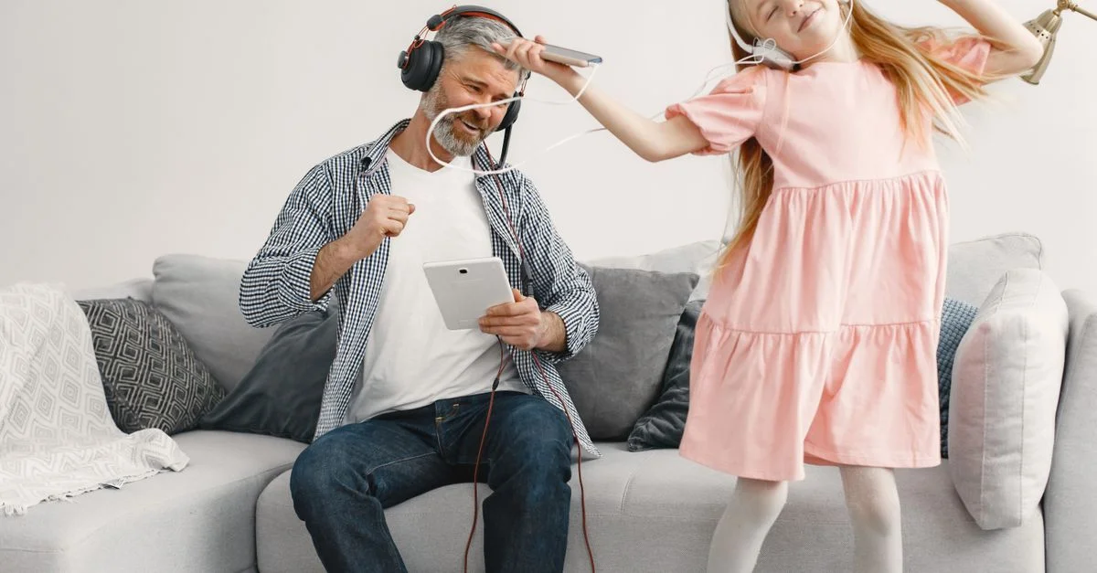Un père et sa fille profitent de la musique en dansant sur le canapé avec des écouteurs dans un salon.