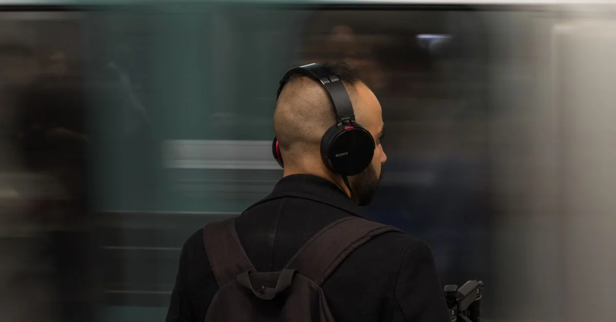Homme portant des écouteurs attend patiemment le train de métro à l'intérieur, créant une sensation de mouvement et de vie urbaine.