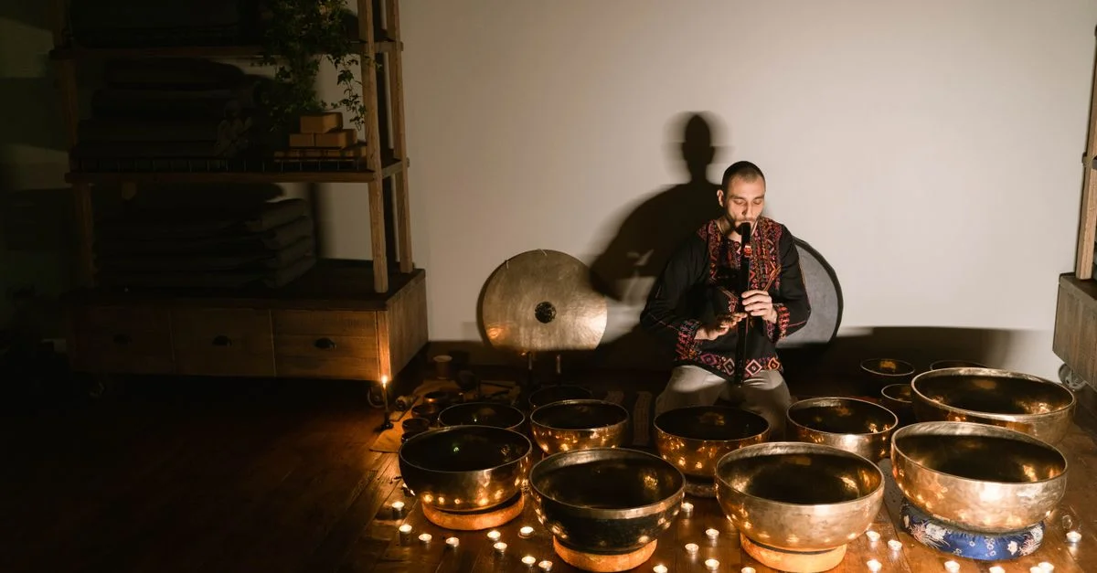 Un homme jouant d'un instrument de musique entouré de bols tibétains, créant une atmosphère relaxante.