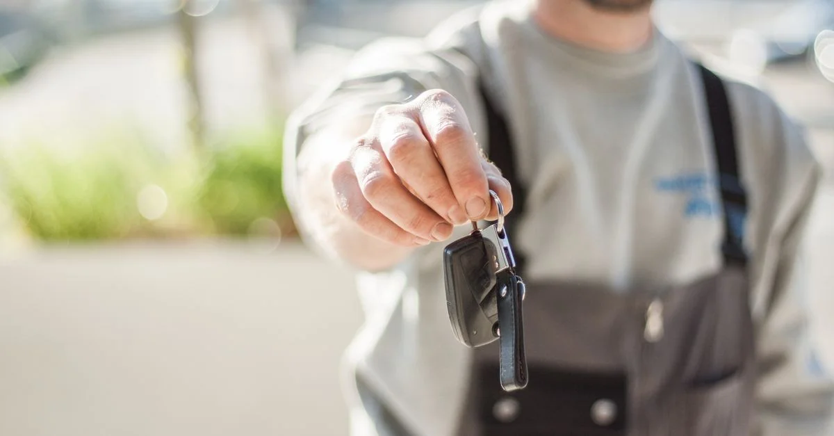 Main tenant une clé de voiture à l'extérieur, arrière-plan flou, mise au point réduite.