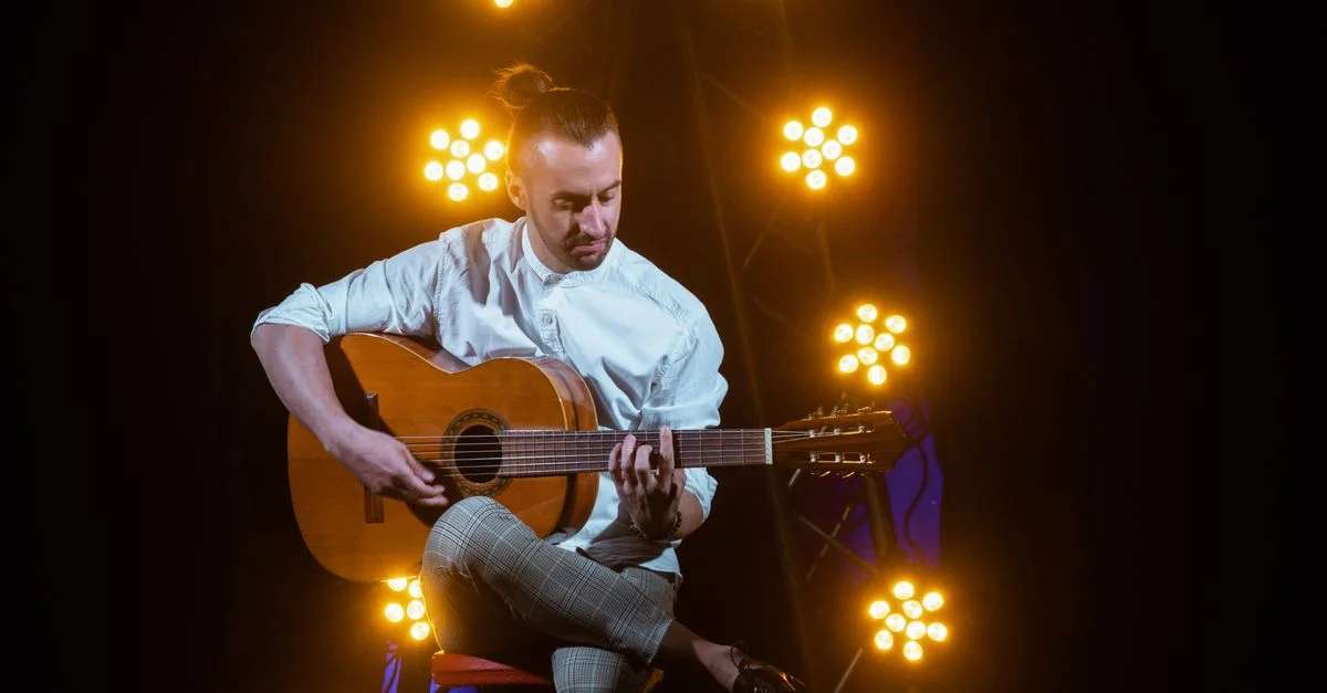 Musicien jouant de la guitare acoustique sur scène. Éclairage dramatique et pose assise.