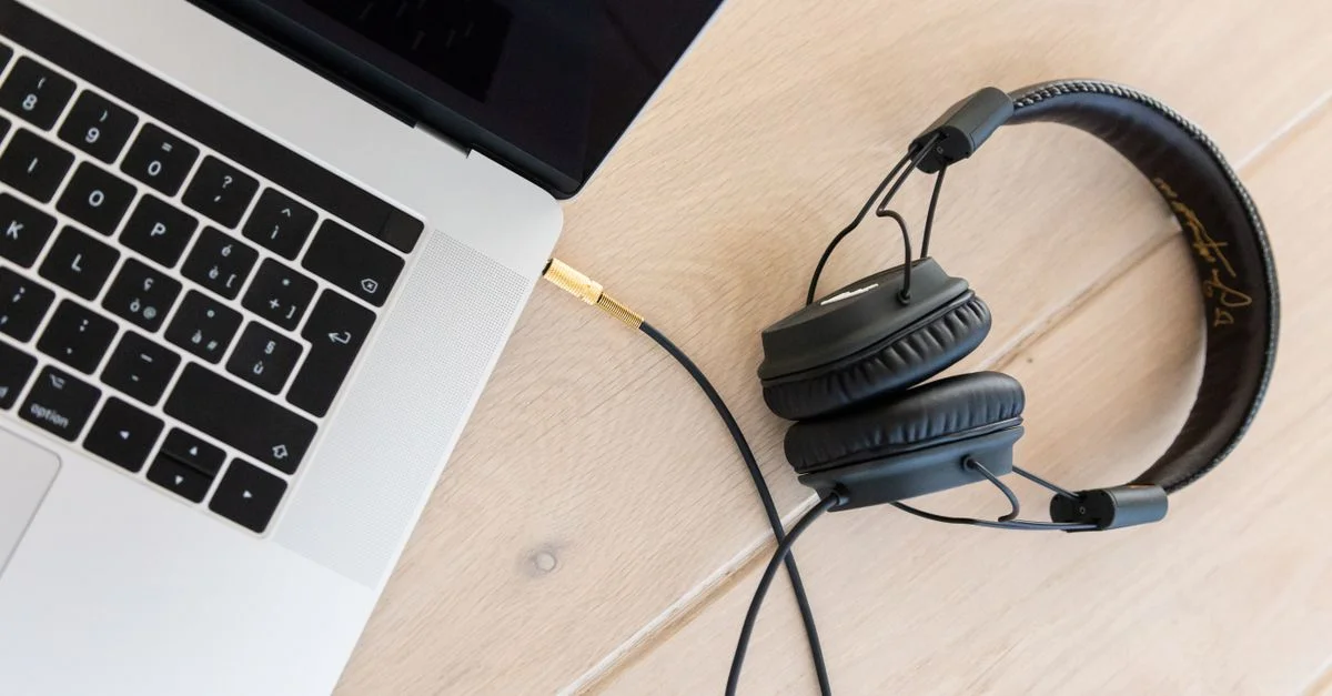 Gros plan d'un ordinateur portable et de casques sur un bureau en bois, mettant en avant la technologie moderne.