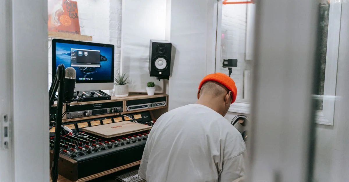 Un homme portant un bonnet est assis et travaille sur du matériel audio dans un studio de musique moderne.